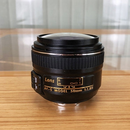 Black fake camera lens model with engraved markings and metal mounting ring