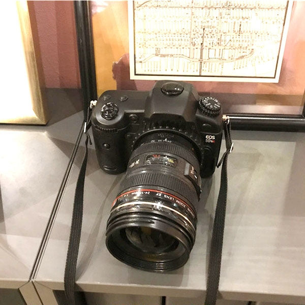 Black dummy DSLR camera prop on display with attached lens and neck strap