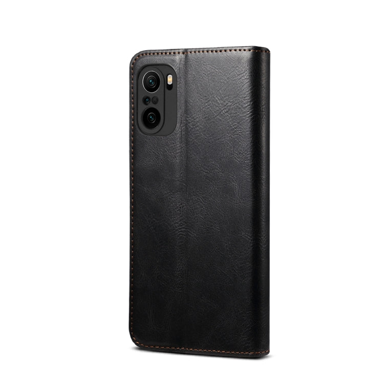 Black leather flip phone wallet case with camera cutout and stitched edges, back view.