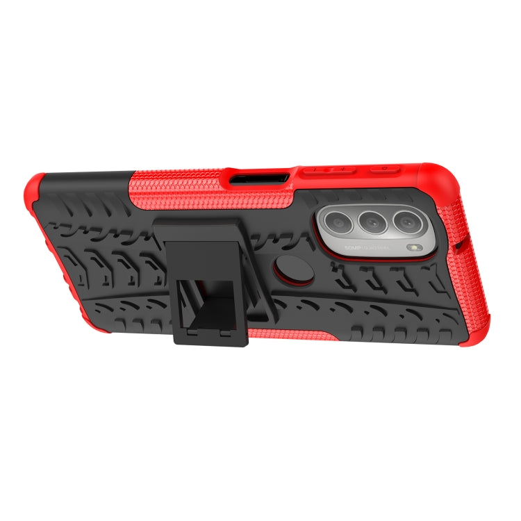 Red and black rugged phone case with tire tread texture, camera cutout, and holder stand