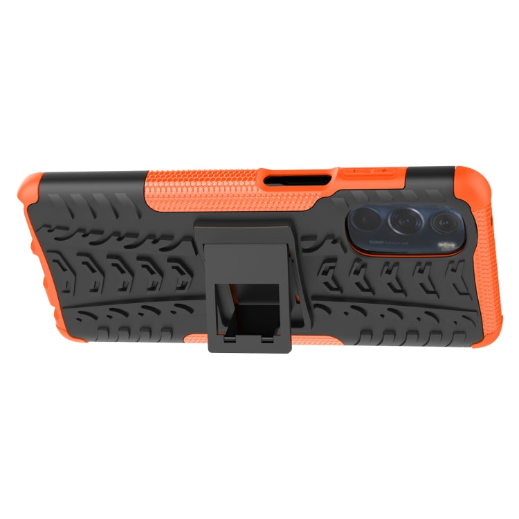 Tire-texture phone case with built-in holder, orange and black back with camera module.