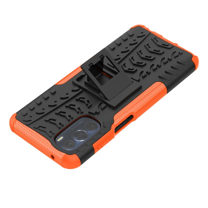 Tire-texture phone case with holder, orange and black diagonal view, camera cutout visible.