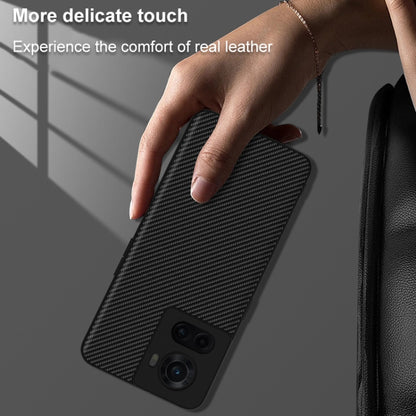 Black carbon-fiber textured phone case for OnePlus 10R/Ace held in hand, camera cutouts