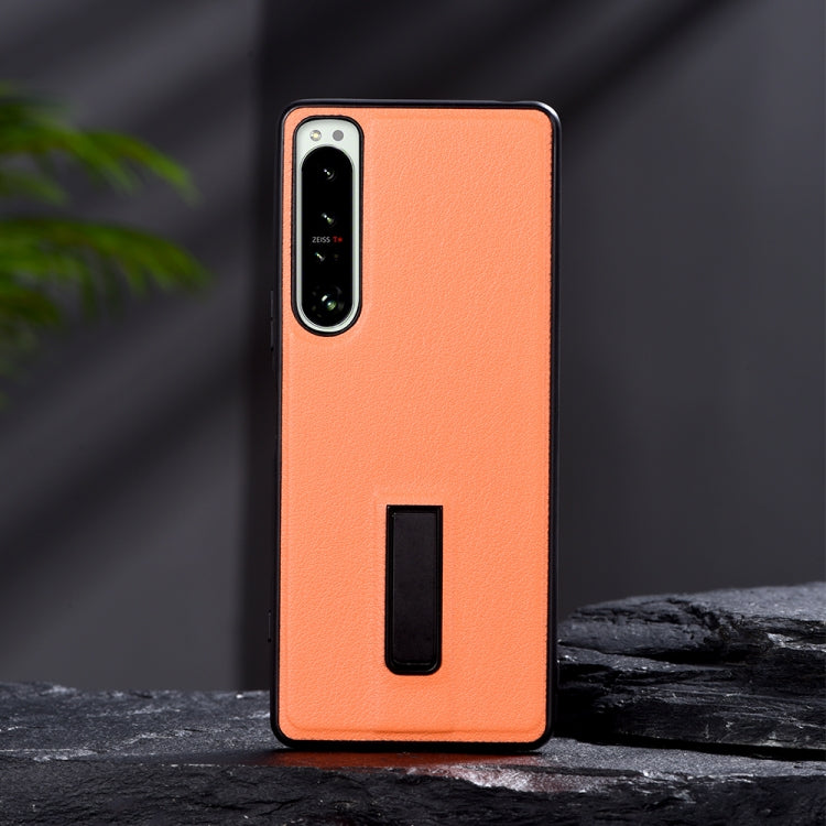 Orange leather-texture protective phone case with metal holder slot and camera cutouts.