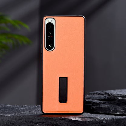 Orange leather-texture protective phone case with metal holder slot and camera cutouts.