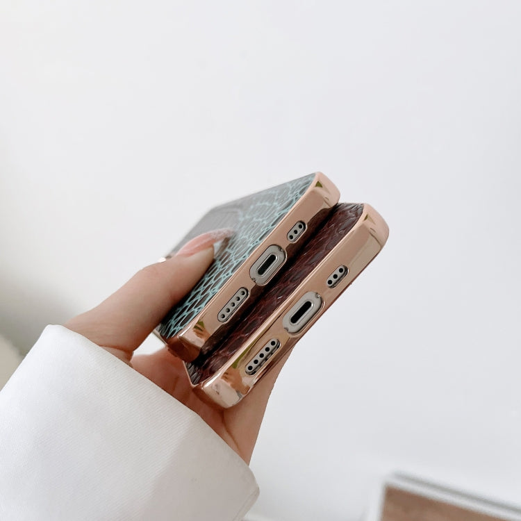 Hand holding crocodile-textured leather phone cases in teal and dark brown