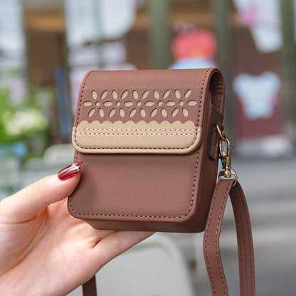 Brown leather crossbody flip phone bag held in hand, with cutout floral panel and strap