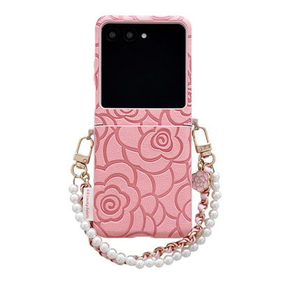 Pink embossed camellia phone case with side buckle and pearl bracelet strap.