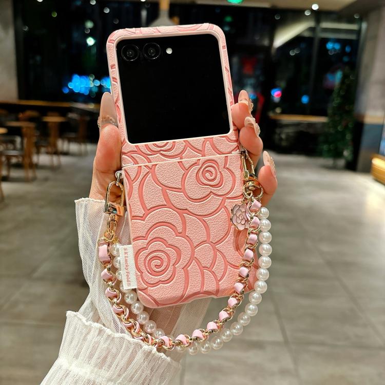 Pink embossed camellia phone case with side buckle and chain pearl bracelet.