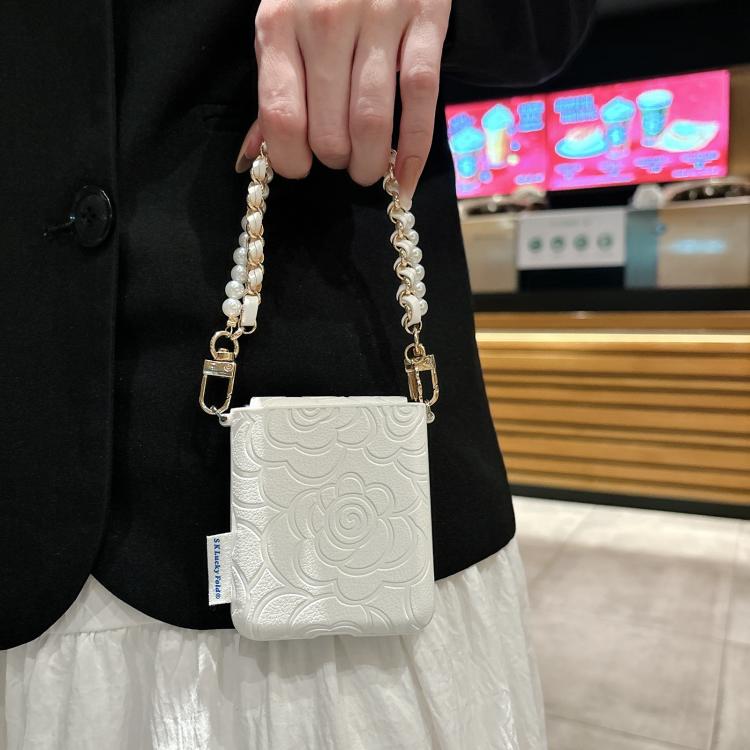 White embossed camellia phone case with side buckle and pearl chain wrist strap.