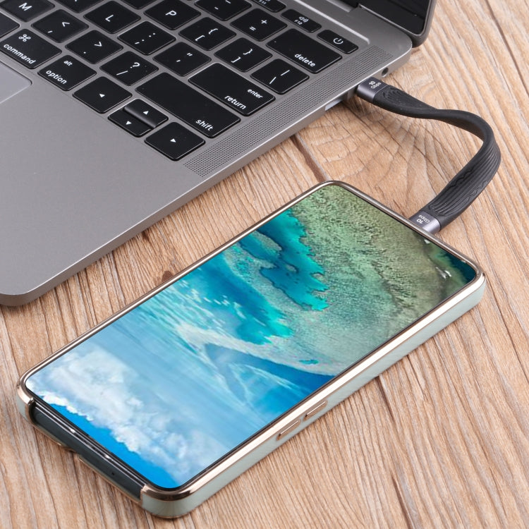 Flat USB-C charging cable connected to a phone and laptop, black with gold ends