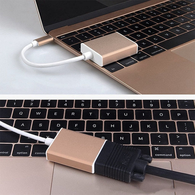 Rose gold USB-C to VGA adapter connected to a laptop keyboard with VGA port.