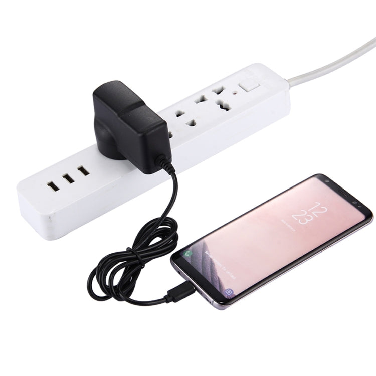 Black micro USB charger cable plugged into power strip beside a smartphone