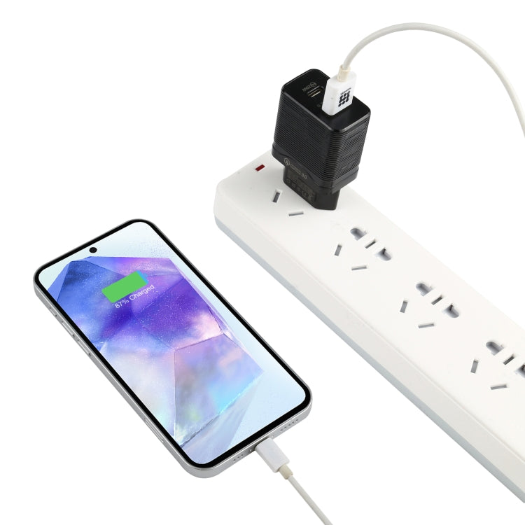 Black travel USB charger plugged into a power strip, charging a smartphone