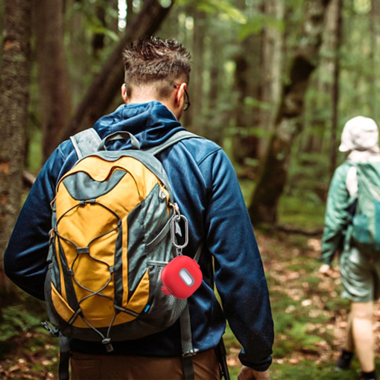 Red earbuds protective case with carabiner attached to backpack while hiking